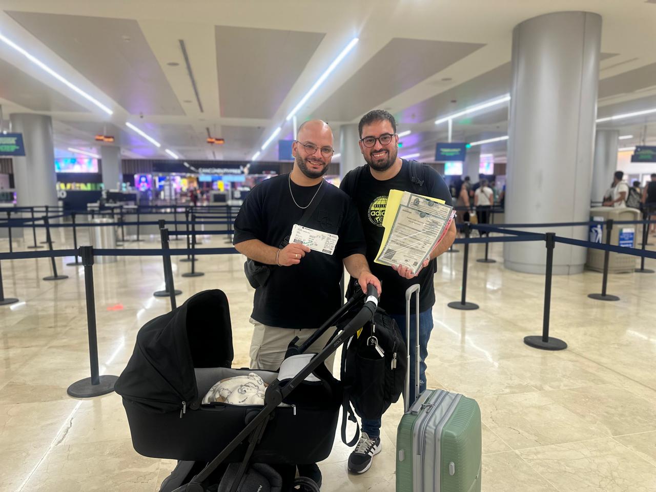 Two dads with their newborn and Amparo birth certificate at Cancún airport