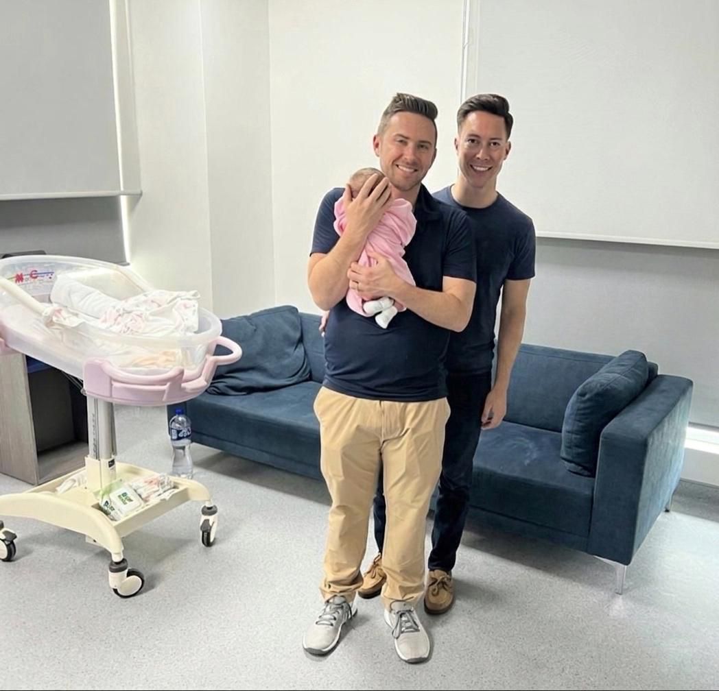 Two fathers holding their newborn baby after a surrogacy program in Mexico